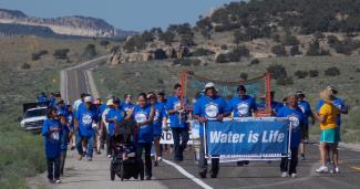 Crowd outdoors in blue shirts marching with Water is Life banner